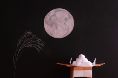黒い背景に月とススキの絵、折り紙で折られたお月見団子を合わせた写真